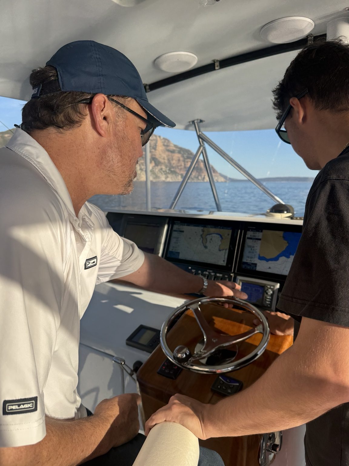 At the helm aboard Decisive with the St Helena coastline beyond